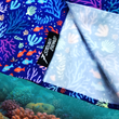 Load image into Gallery viewer, Bottom sweep tag area shot of the 7-Strong "Coral of the Story" adult button down shirt. Color of the shirt is blue with vibrant purple, teal, orange sea life imagery - particularly fish and coral reef. The shirt is shown against an underwater background showcasing coral.