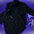 Load image into Gallery viewer, Full of the 7-Strong "Flux Capacity" short sleeve and long sleeve button downs overlapping each other, showcasing bursts and lines of purple light peering through a black grid of cubes. The background is of a fashion show runway in purple hue.