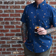 Load image into Gallery viewer, Adult male model, holding an Old Fashioned and wearing "Call Me Old Fashioned" adult short sleeve button-down. Features elements of an Old Fashioned cocktail (bottle of bourbon, glasses, oranges, stirrers, and ice) against a blue background which faintly spells out an Old Fashioned recipe. Model is against a brick wall.