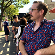 Load image into Gallery viewer, Medium close up of a male of medium build, model wearing 7-Strong Aye Poppy shirt out in public, staring off. Shirt features an array of red poppies and white sprigs against a deep navy blue background.