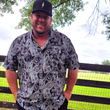 Load image into Gallery viewer, Male model wearing the adult 7-Strong "Cinco de Mayhem" button down shirt. Shirt features black and white posters featuring various created luchadors advertised for matches, all overlapping each other over a black shirt. Model is outside against a fence.