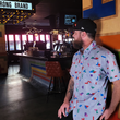 Load image into Gallery viewer, Medium shot of adult male in the 7-Strong Block Party adult button down, featuring various colored blocks of different arrangements inspired by a classic video game, cascading down the shirt against a grayish background featuring shadows of the same shapes. Model is posed in the lobby of an arcade with "7-STRONG BRAND" on its marquee.