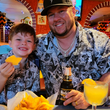 Load image into Gallery viewer, Father and son at a Mexican restaurant smiling at camera wearing the youth and adult adult 7-Strong "Cinco de Mayhem" button down shirt. Shirt features black and white posters featuring various created luchadors advertised for matches, all overlapping each other over a black shirt.