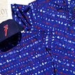 Load image into Gallery viewer, Full, front faing shot of the 7-Series trucker hat, showcasing its all navy blue look, back mesh panel, red puffed embroidered 7 with white outline, against a background of the Declaration of Independence, laid on top of both the youth and adult versions of the 1776 royal blue shirt with Americana icons striped throughout .