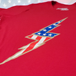 Load image into Gallery viewer, Angle middle view of the red Freedom Bolt unisex tee, featuring a large center placed 7-bolt, outlined in gold, with white stars on blue on top and red and white stripes on the bottom. The shirt is featured on a U.S. flag background.