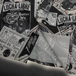 Load image into Gallery viewer, Bottom sweep tag view of the youth 7-Strong "Cinco de Mayhem" button down shirt. Shirt features black and white posters featuring various created luchadors advertised for matches, all overlapping each other over a black shirt. Shirt is displayed on a black gradient background with some of the characters ghosted in the back.