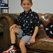 Load image into Gallery viewer, Male youth modeling the youth short sleeve version of "Got 'Em!" The button down features various athletic fashion sneakers in an 8-bit format arranged all over a black shirt. Child is sitting on a coach looking at camera, while on the right is detail circle showcasing various shoes designed on the shirt.