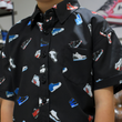 Load image into Gallery viewer, Midsection close up of male child model wearing the youth short sleeve version of "Got 'Em!" The button down features various athletic fashion sneakers in an 80bit format arranged all over a black shirt. The model is standing in a room with visible sneakers displayed behind him.