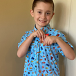 Load image into Gallery viewer, Child model wearing the 7-Strong "Cheat Day" youth button down featuring various snacks, treats, and fast food features on a light blue shirt hiding candy in the shirt pocket.