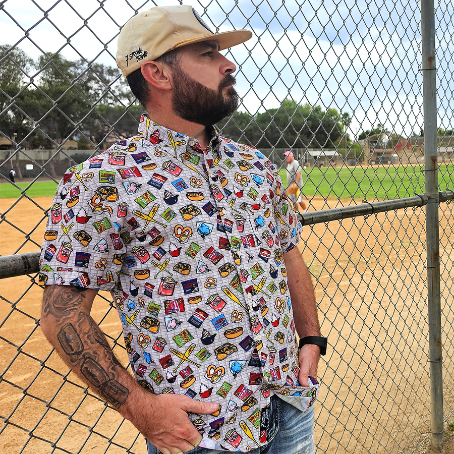 Man wearing a colorful patterned shirt and beige cap standing near a chain-link fence.