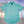 Load image into Gallery viewer, Full centered view of the adult 7-Strong &quot;Sunset Palms&quot; shirt, featuring small yellow and pink suns, reminiscent of a sunset, behind a silhouette of a palm tree and birds, patterned at various angles all over the turquoise-like shirt. The shirt is featured against a photo of a palm tree beach at sunset.
