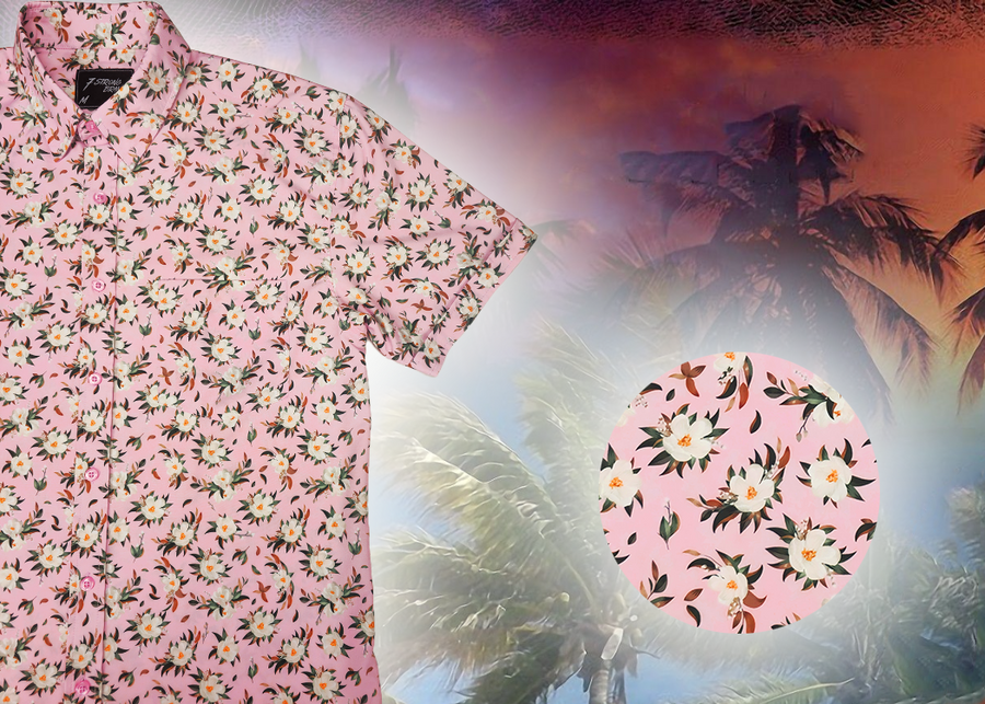 3/4 Close Up view of the "Magnolia PI" 7-Strong Adult button down shirt, featuring white and green magnolia flowers patterned all over a light pink background. The shirt itself is displayed against a palm tree tropical background. The bottom left features a detail circle showing a close up of the shirt's floral design. 