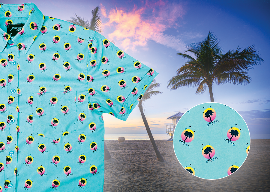 A 3/4 view of the adult 7-Strong "Sunset Palms" shirt, featuring small yellow and pink suns, reminiscent of a sunset, behind a silhouette of a palm tree and birds, patterned at various angles all over the turquoise-like shirt. The shirt is featured against a photo of a palm tree beach at sunset. Bottom right corner features a close up circle detailing the shirt design.  