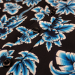 Load image into Gallery viewer, Midsection button view of the 7-Strong adult Electric Palms shirt, a collection of electric blue palm fronds featured against a black shirt. Shirt is displayed against a scenic beach background. 
