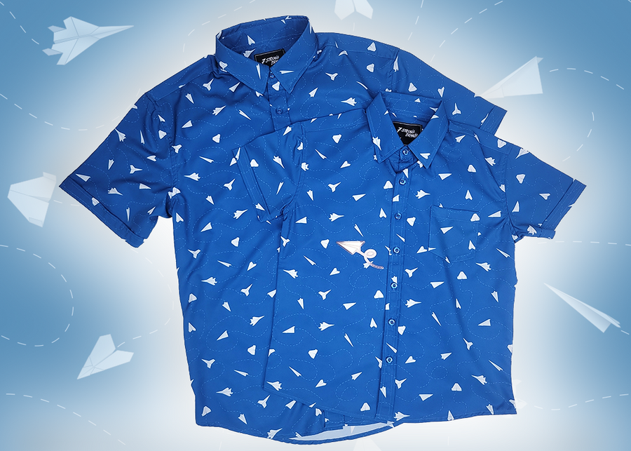 A complete view of the adult and youth 7-Strong "Paper Planes" button down shirts overlapping one another - featuring various sizes and designs of paper airplanes, some with dotted trails behind them against a royal blue background. The shirt is displayed against a faced background of the shirt details.
