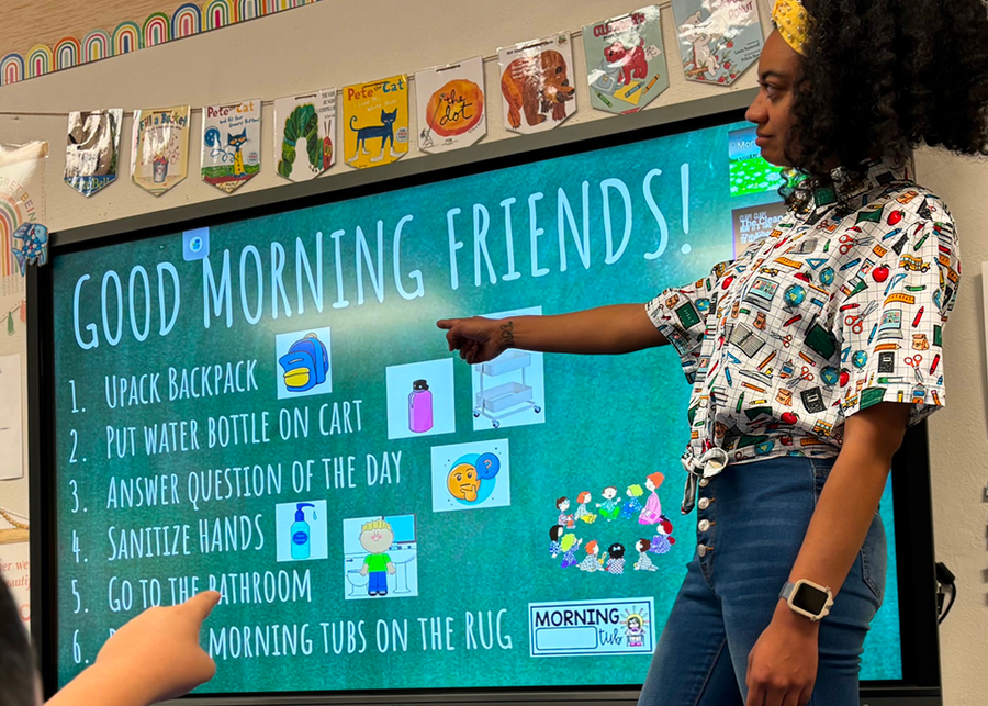 Female model wearing the 7-Strong Class Act button down while teaching a class and pointing towards an electronic blackboard. 