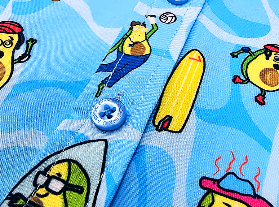 Midsection button view of the 7-Strong Avocado Coast button down featuring various avocado characters engaging in summer activities such as grilling, playing volleyball, weightlifting, surfing, etc against a blue shimmery wave looking background. 