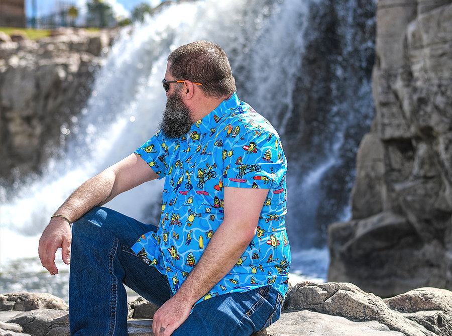 Male model sitting on a rock looking over his shoulder at a waterfall wearing the 7-Strong Avocado Coast button down. 