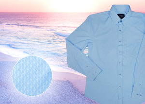 Close up mid button view of the baby blue long sleeve EveryWEAR adult button up. Pattern is subtle white 7-Bolts lined up all against each other across a baby blue background. The shirt is featured on a soft background of a wave hitting the beach. Bottom left corner features a detail circle showing close ups of the subtle 7-bolts on the shirt. 