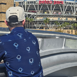 Male model, back turned to camera looking at baseball stadium in distance wearing 7-Strong's Ballpark Blueprint collaboration shirt featuring overhead maps of major league stadiums. 