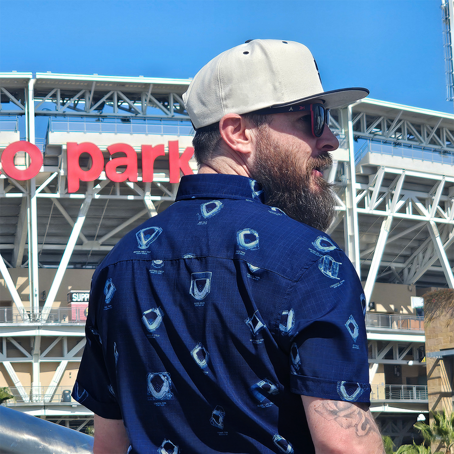 Male model in front of a baseball stadium wearing 7-Strong's adult Ballpark Blueprints shirt, featuring overhead maps of all the major league stadiums.