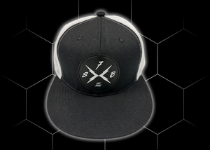 Close up centered shot of the 7-Strong black "Branded" trucker hat with raised X-Badge patch centered on the front of the hat. Product is featured against a black geometric background. 