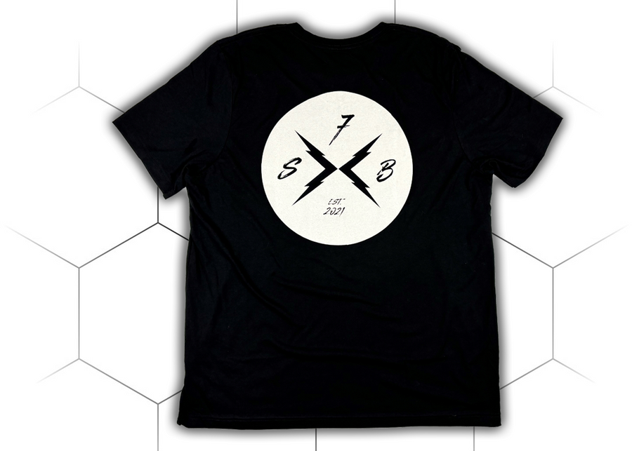 Centered full view of the back of the 7-Strong black Branded tee, featuring the X-Brand patch logo centered in white. Shirt is featured against a white geometric background. 