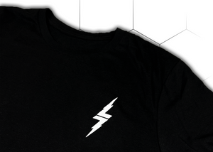 Front top of shoulder, left lapel look of the 7-Strong black Branded tee, featuring a 7-bolt left justified in white. Shirt is featured against a white geometric background.