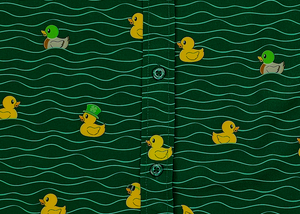 A centered close up, midsection view of the 7-Strong "Duck O' The Irish" adult button down, featuring a deep green water-replicating background with various rubber ducks swimming along the waves. 