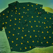 Load image into Gallery viewer, A centered, overlapping view of the 7-Strong &quot;Duck O&#39; The Irish&quot; adult and youth button down, featuring a deep green water-replicating background with various rubber ducks swimming along the waves. The shirt is featured against a green river scenic with a giant inflatable duck in the background.
