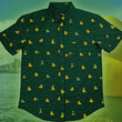 Load image into Gallery viewer, A centered view of the 7-Strong &quot;Duck O&#39; The Irish&quot; adult button down, featuring a deep green water-replicating background with various rubber ducks swimming along the waves. The shirt is featured against a green river scenic with a giant inflatable duck in the background.
