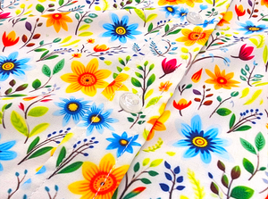 A midsection close-up shot of the 7-Strong "Daisy Me Rollin'" adult button down shirt, a white base color with various blue, red, orange, and yellow floral daisies in an all over print. The shirt is displayed against a background of a field of daisies.