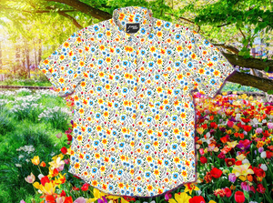 A full, centered close-up shot of the 7-Strong "Daisy Me Rollin'" adult button down shirt, a white base color with various blue, red, orange, and yellow floral daisies in an all over print. The shirt is displayed against a background of a field of daisies.