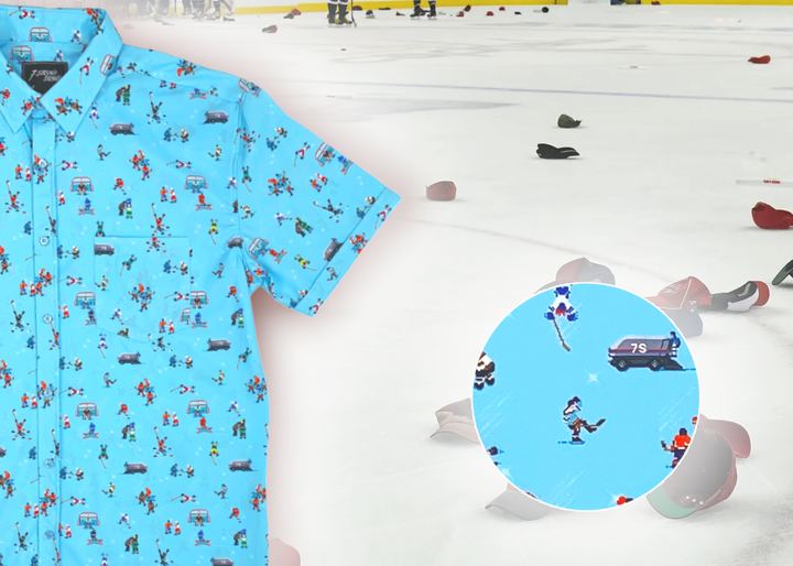 A 3/4 full view of the adult 8-Bit Hat Trick button down - featuring various 8-bit inspired scenes from hockey games on a light blue ice-like background. The shirt is featured against a ice hockey floor with hats strewn about. The bottom right features a detail circle with a close up of a few scenes from the shirt. 