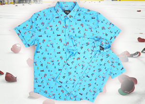A full, centered, overlapping view of the youth and adult 8-Bit Hat Trick button down - featuring various 8-bit inspired scenes from hockey games on a light blue ice-like background. The shirt is featured against a ice hockey floor with hats strewn about. 