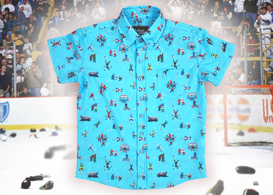 A full, centered view of the youth 8-Bit Hat Trick button down - featuring various 8-bit inspired scenes from hockey games on a light blue ice-like background. The shirt is featured against a ice hockey floor with hats strewn about.