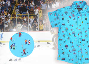 A 3/4 full view of the youth 8-Bit Hat Trick button down - featuring various 8-bit inspired scenes from hockey games on a light blue ice-like background. The shirt is featured against a ice hockey floor with hats strewn about. The bottom left features a detail circle with a close up of a few scenes from the shirt. 