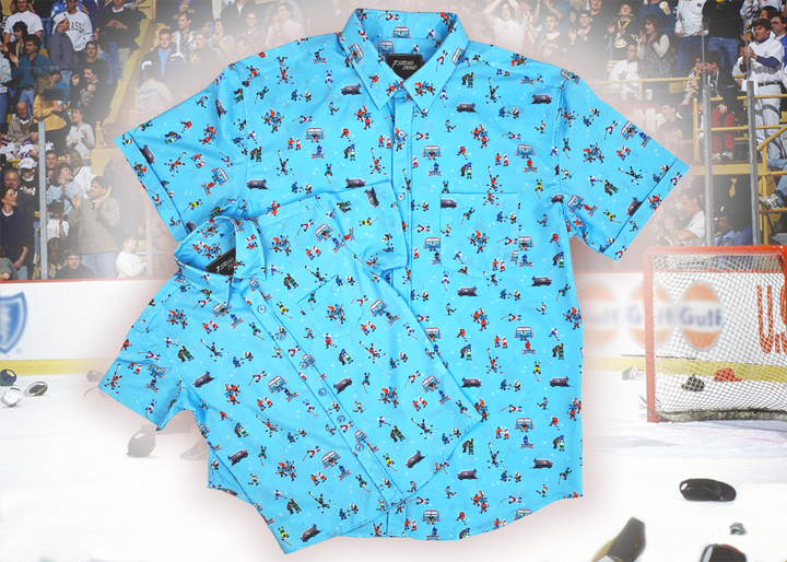A full, centered, overlapping view of the youth and  adult 8-Bit Hat Trick button down - featuring various 8-bit inspired scenes from hockey games on a light blue ice-like background. The shirt is featured against a ice hockey floor with hats strewn about. 