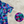 Load image into Gallery viewer, 3/4 close up view of the 7-Strong &quot;Neon Coast&quot; adult button down shirt. Featuring vibrant teal, pink, and blue palm fronds, overlapping throughout the shirt,  against a black/deep purple background. The shirt is laid out on the sand of a beach. In the bottom right corner, there is a detail circle featuring a close up of the shirt&#39;s design.  
