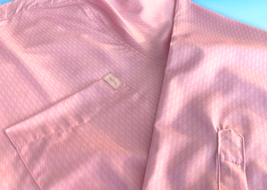 Close up pocket view of the pink long sleeve EveryWEAR adult button up. Pattern is subtle white 7-Bolts lined up all against each other across a pink background. The shirt is featured on a soft background of a wave hitting the beach. 