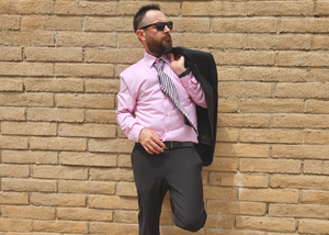 Medium view of a male model sporting the pink long short sleeve EveryWEAR adult button up, matched with a black suit. Pattern is subtle white 7-Bolts lined up all against each other across a pink background.