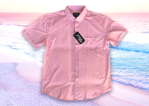 Full centered view of the pink short sleeve EveryWEAR adult button up. Pattern is subtle white 7-Bolts lined up all against each other across a pink background. The shirt is featured on a soft background of a wave hitting the beach.