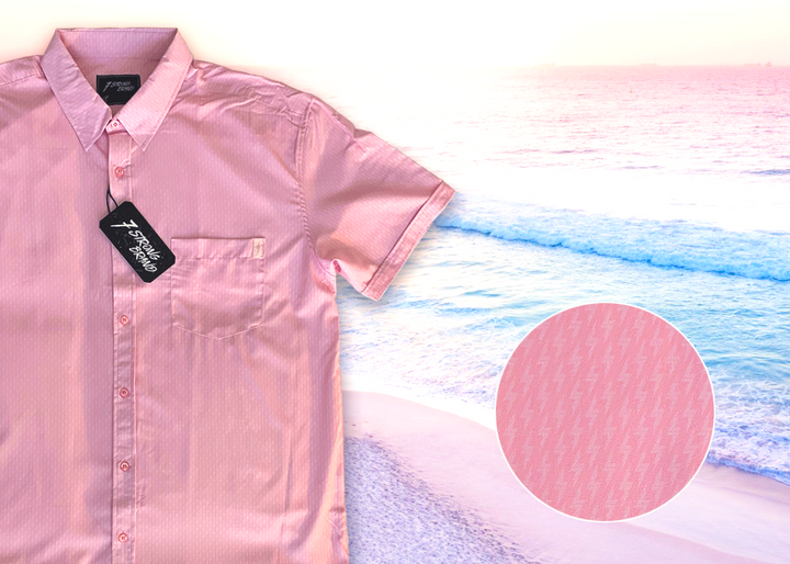 3/4 full view of the pink short sleeve EveryWEAR adult button up. Pattern is subtle white 7-Bolts lined up all against each other across a pink background. The shirt is featured on a soft background of a wave hitting the beach. Bottom right corner features a detail circle of the bolts up close.