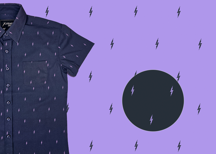 3/4 view of the youth 7-Strong Slate 7-Bolt short sleeve shirt, featuring lavender 7-bolts interspersed on a slate gray background. The shirt is featured on a lavender backdrop with black bolts. The bottom left features a detail circle showing the 7-bolt design up close.