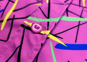 A midsection button view of the 7-Strong youth "Strongfetti" button down, a bold pink shirt featuring black, yellow, lime green, and navy blue scratches that appear like confetti falling from the sky. The shirt is featured on a white background with colorful falling confetti.