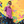 Load image into Gallery viewer, A shot of a male youth model wearing the 7-Strong youth &quot;Strongfetti&quot; button down, a bold pink shirt featuring black, yellow, lime green, and navy blue scratches that appear like confetti falling from the sky. The model is standing against a colorful paint-splatter design wall peering into the camera. 
