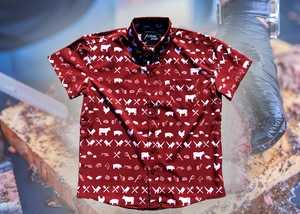 A full, centered view of the 7-Strong youth "Smoke Show" button up, a deep maroon red colored shirt with rows of various barbecue and cookout related items and delicacies silhouetted in white. The shirt is displayed against a background of a brisket being pulled.