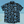 Load image into Gallery viewer, Full view of the 7-Strong youth Electric Palms shirt, a collection of electric blue palm fronds featured against a black shirt. Shirt is displayed against a scenic beach background.
