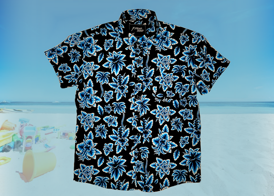 Full view of the 7-Strong youth Electric Palms shirt, a collection of electric blue palm fronds featured against a black shirt. Shirt is displayed against a scenic beach background.