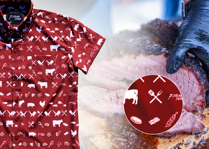 A 3/4 full view of the 7-Strong youth "Smoke Show" button up, a deep maroon red colored shirt with rows of various barbecue and cookout related items and delicacies silhouetted in white. The shirt is displayed against a background of a brisket being pulled. The bottom right features a detail circle showing a close-up of elements in the design. 